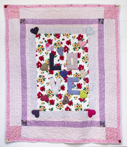 Quilt with central panel reading LOVE on a floral background, with pink and purple bands around it.