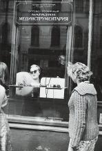 black and white photo of two women looking in the window of an eyeglass shop