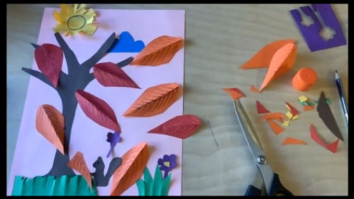 Paper collage of leaves on a tree with scissors and paper scraps beside the collage
