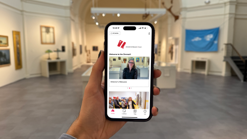 Hand holding an iPhone displaying the Zimmerli's Bloomberg Connects guide homepage with the Art of the Americas gallery in background.