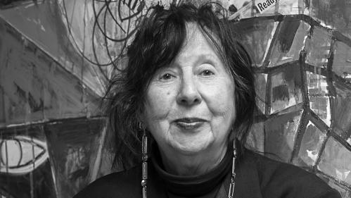 Jaune Quick-to-See Smith, an older Native American woman, stands with her arms crossed dressed in all black.