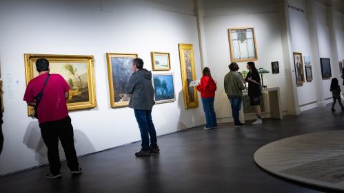 People look at art hung on the walls of a gallery.