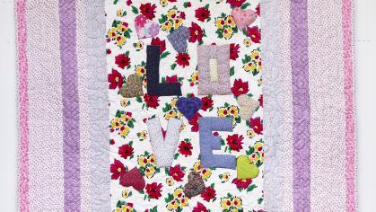 Quilt with central panel reading LOVE on a floral background, with pink and purple bands around it.