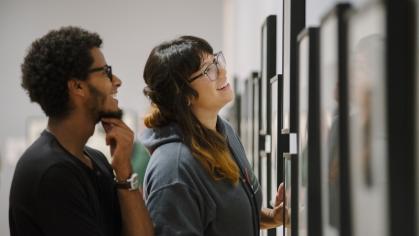 A man and woman look at photos on a wall