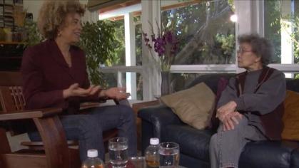 Angela Davis and Yuri Kochiyama sit in a living room conversing together.