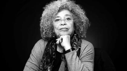 Black and white portrait of Angela Davis, an older Black woman wearing glasses, with her chin resting on her left hand