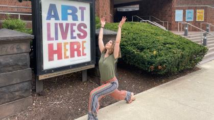 Photo of woman doing a yoga pose outside the Zimmerli Art Museum, next to a sign reading Art Lives Here.