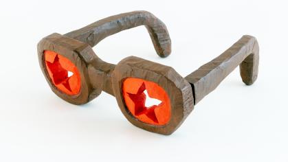 Carved and painted wooden glasses with brown frames and star cutouts in the red lenses 