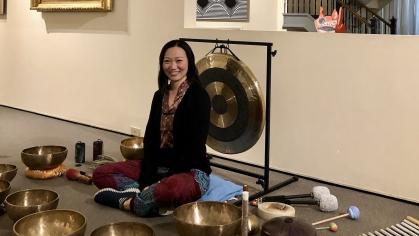 Asian woman sitting in gallery with meditation sound bowls