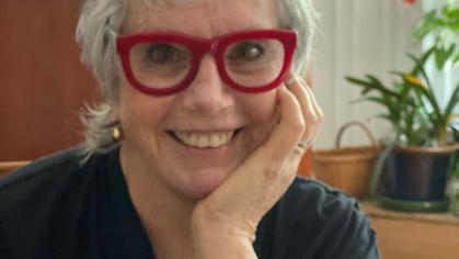 headshot of white woman with short silver hair and red glasses, smiling