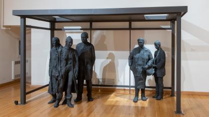 six plaster cast figures painted black stand under a bus shelter