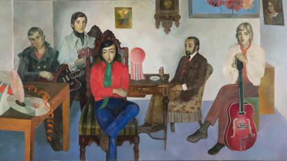 Various individuals sit in a living room with white walls and a blue floor.