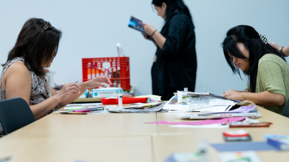People working on art at a table. Text in the top left reads out the event name and information.