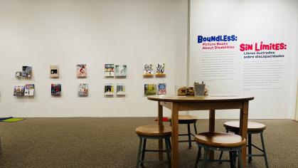 Table and chairs with books on holders mounted to a white wall.