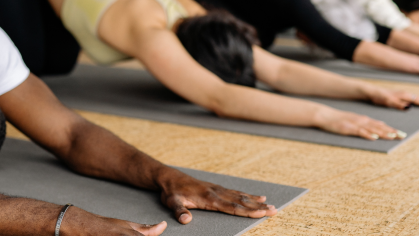 Various people perform downward dog on yoga mats in a brightly lit studio.