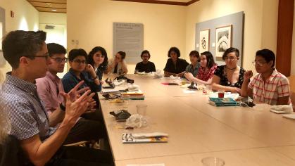 Artist Alison Bechdel sits at a long table talking with university students 