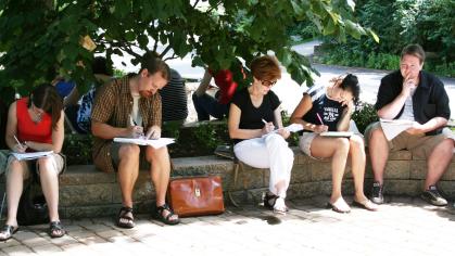People sit outside on a low brick wall, each writing on clipboards.
