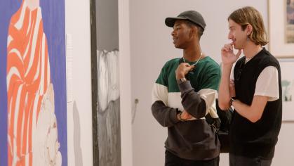 Two people look at artwork on the wall of a gallery.