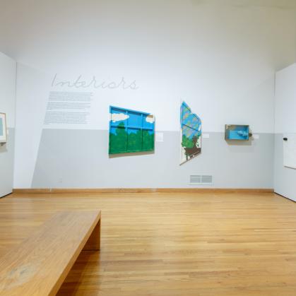 View of gallery; wall text says Interiors; artwork includes three painted window-like shapes and a painted red door