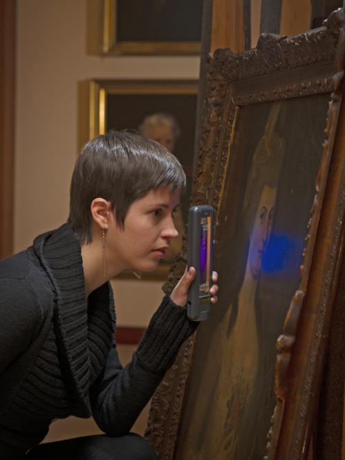 Intern Kate Scott examining a painting with a magnifying glass