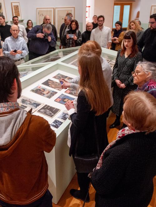 A crowd stands around a case in a gallery listening to a curator