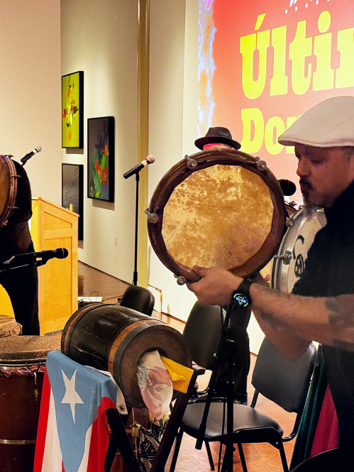 Band plays in an art gallery. The members hold instruments like drums, guitars, and microphones.