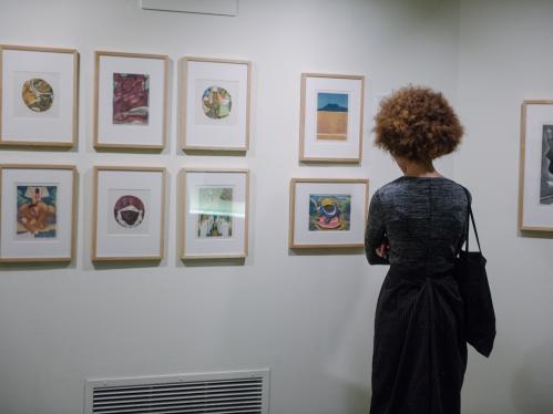 A woman, seen from behind, looks at prints hanging on a wall