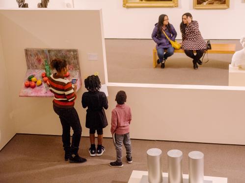 A family looks at art together while on the other side of a low wall, two women sit on a bench and talk.