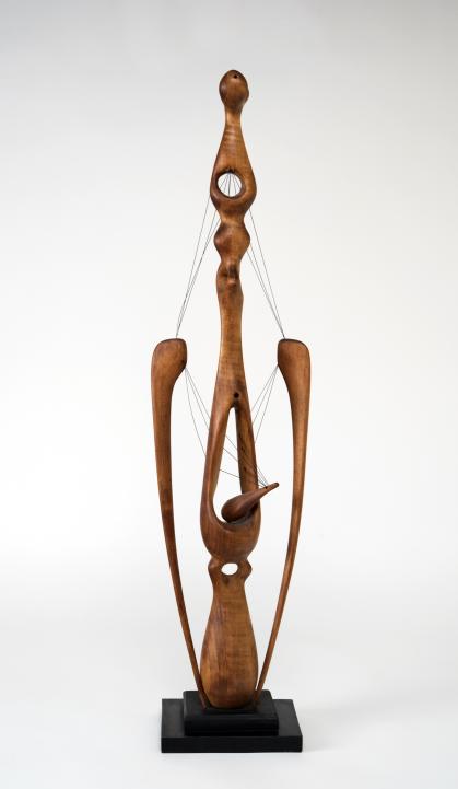 Carved wooden sculpture with two long spider-leg like shapes attached to a tall central shape by thread