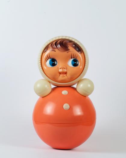 Children's toy with round doll head and a red sphere for a body with two short rounded arms.