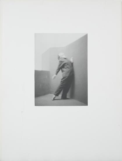 Photo of a figure posed against a wall, leaning back dramatically with head looking up and arm extended behind them