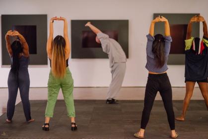 Five people stand in a museum gallery, stretching their arms over their heads