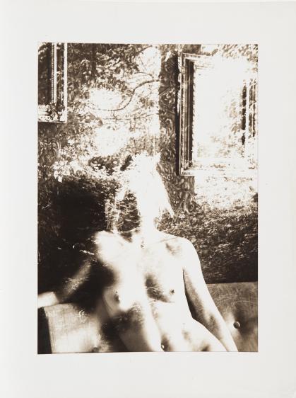 Photo of nude woman sitting on a couch; head and upper part of photo are obscured by a pattern of light and shadow