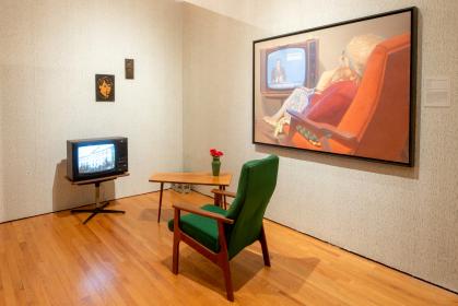 Room with green armchair and table in front of an old TV; a painting with a similar arrangement hangs on the wall
