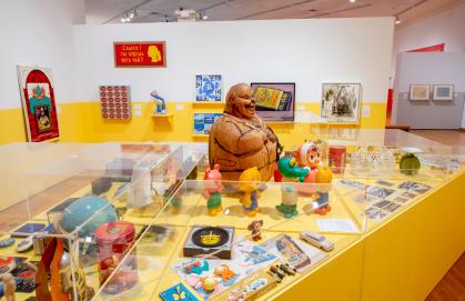 Installation view of Everyday Soviet with case of toys and trinkets, with paintings on the walls