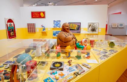 Installation view of Everyday Soviet with case of toys and trinkets, with paintings on the walls
