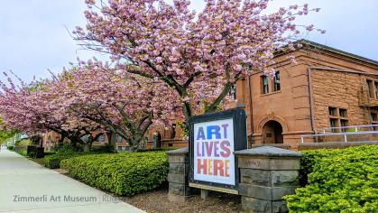 Photo of Voorhees Hall seen from right with cherry blossoms and sign reading "Art Lives Here"