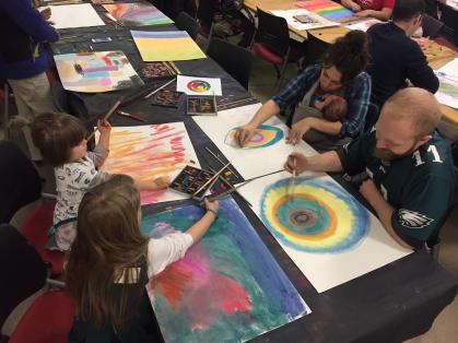 A family works on an art project together, drawing with pastels.