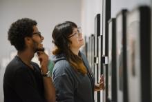 A man and woman look at photos on a wall
