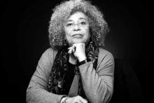 Black and white portrait of Angela Davis, an older Black woman wearing glasses, with her chin resting on her left hand