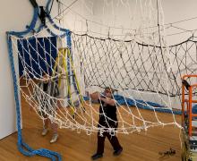 artist in gallery surrounded by installation of rope tunnel