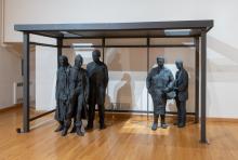six plaster cast figures painted black stand under a bus shelter