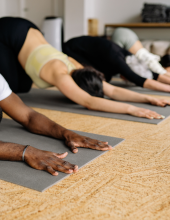 Various people perform downward dog on yoga mats in a brightly lit studio.