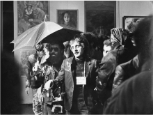 Group of sharply dressed people walk through what appears to be an art gallery.