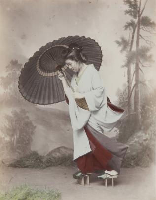 Handcolored studio photo of young Japanese woman holding a parasol against a gust of wind