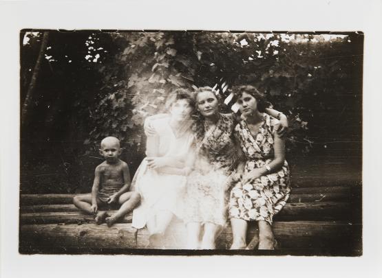 Photo of three women sitting on a stack of logs beside a young boy; a ghostly white light bisects the image