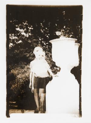 Two superimposed photos of the same young boy standing besides a large urn which is all in white
