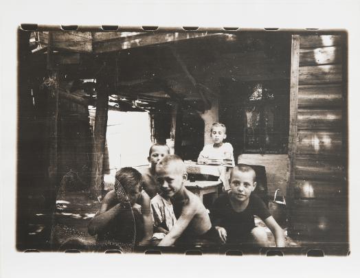 Black and white photo of five light-skinned boys sitting under a porch roof; the film edges are visible