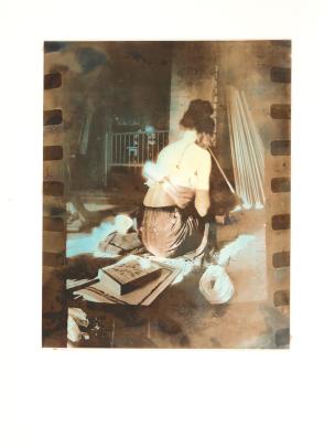 Photo of woman seen from behind seated in a room with books and other materials