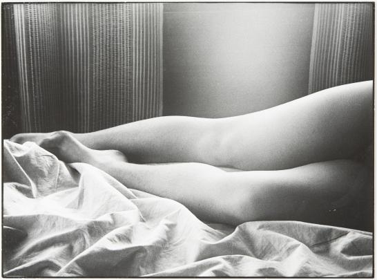 B&W photo of a woman's bare legs lying on a rumpled sheet